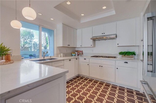 kitchen with a tray ceiling, stainless steel gas cooktop, hanging light fixtures, white cabinets, and sink