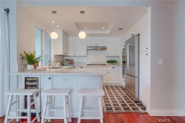 kitchen featuring kitchen peninsula, a breakfast bar area, a tray ceiling, high quality fridge, and sink