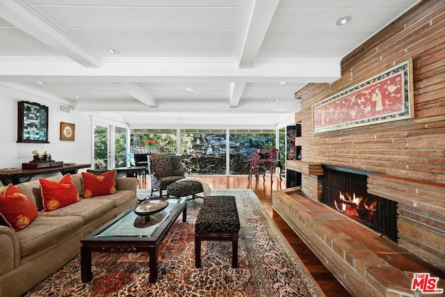 living room with hardwood / wood-style flooring, a brick fireplace, and beamed ceiling