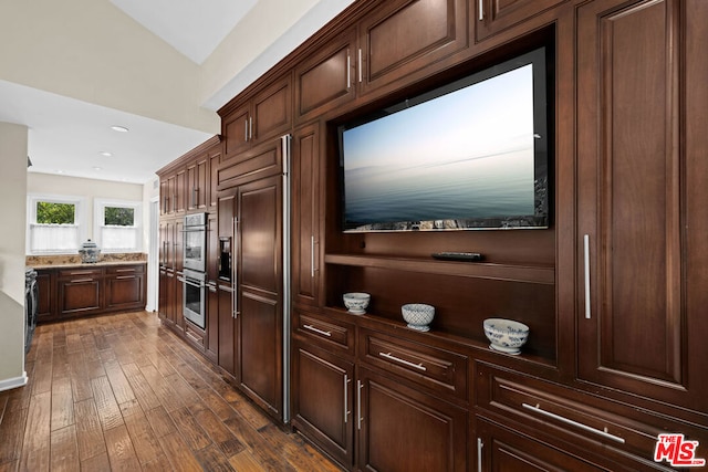 kitchen with dark brown cabinetry, dark hardwood / wood-style floors, paneled built in fridge, and double oven