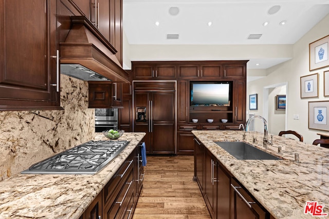 kitchen with sink, light hardwood / wood-style flooring, premium range hood, appliances with stainless steel finishes, and light stone counters