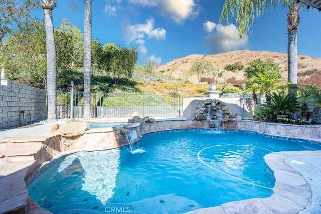 view of swimming pool featuring pool water feature, a mountain view, and an in ground hot tub