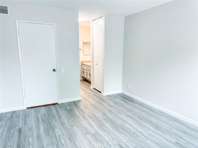 unfurnished bedroom featuring ensuite bathroom and light wood-type flooring