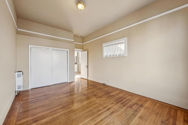 unfurnished bedroom featuring heating unit, radiator, a closet, and hardwood / wood-style floors