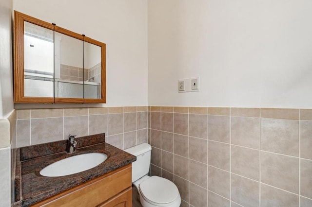 bathroom with toilet, vanity, and tile walls