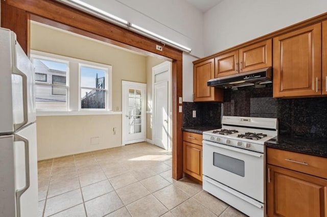 kitchen with light tile patterned floors, backsplash, dark stone countertops, and white appliances