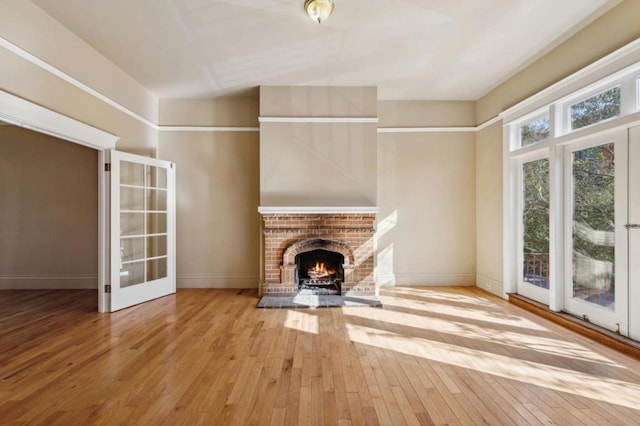 unfurnished living room with light wood-type flooring, french doors, and a fireplace