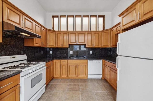 kitchen with light tile patterned floors, backsplash, white appliances, dark stone countertops, and sink