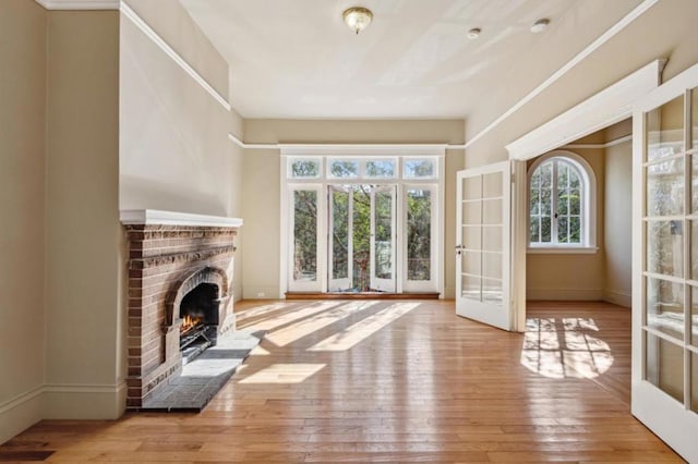 unfurnished living room with french doors, a brick fireplace, and light hardwood / wood-style flooring