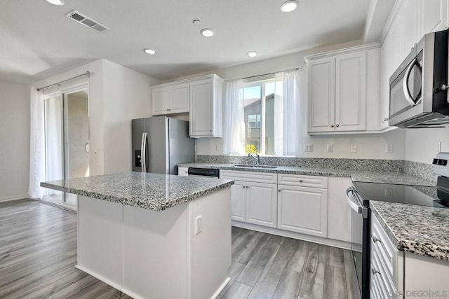 kitchen with light wood-type flooring, stainless steel appliances, sink, white cabinets, and a kitchen island