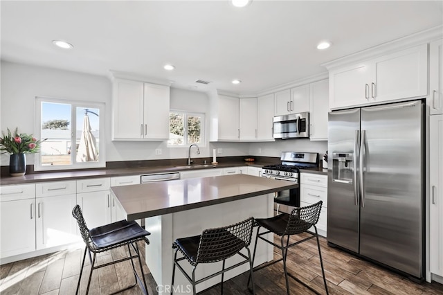 kitchen with stainless steel appliances, sink, white cabinets, a center island, and a kitchen bar