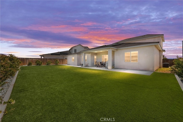 back house at dusk featuring a patio and a yard