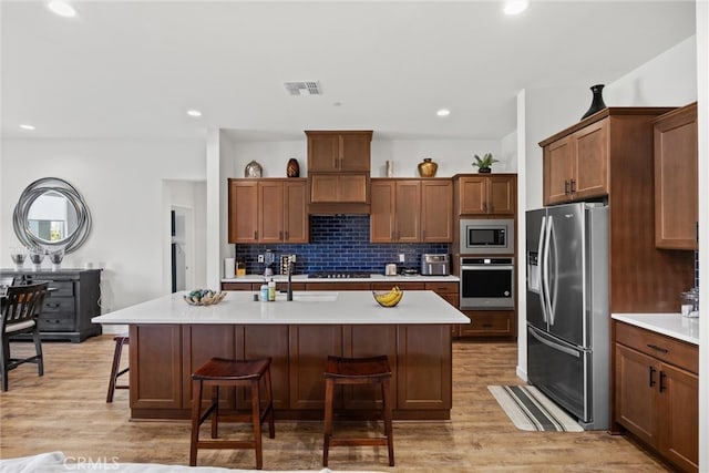 kitchen with light hardwood / wood-style flooring, a kitchen island with sink, stainless steel appliances, and a breakfast bar area