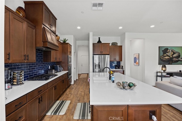 kitchen with stainless steel fridge, black gas cooktop, a kitchen island with sink, light wood-type flooring, and sink