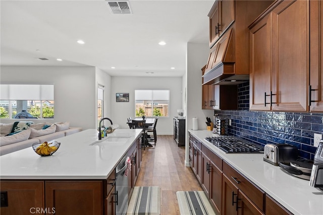 kitchen featuring an island with sink, sink, light wood-type flooring, premium range hood, and appliances with stainless steel finishes