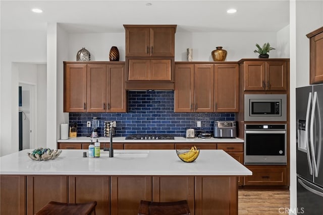 kitchen with a kitchen bar, stainless steel appliances, light wood-type flooring, and an island with sink