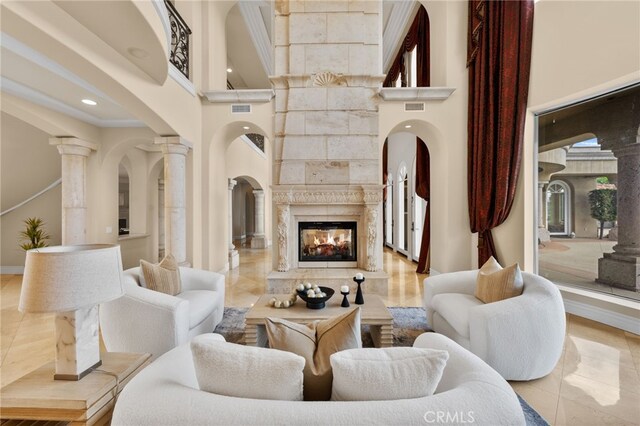 living room featuring a multi sided fireplace, a towering ceiling, ornamental molding, light tile patterned floors, and decorative columns