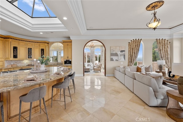 interior space with light stone countertops, backsplash, a skylight, crown molding, and a breakfast bar area