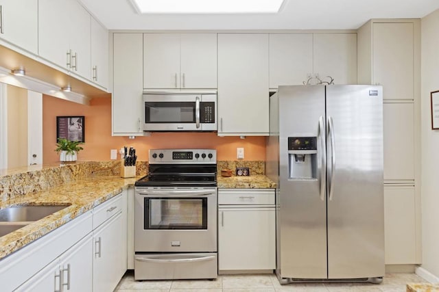 kitchen with light stone countertops, white cabinetry, light tile patterned flooring, and stainless steel appliances