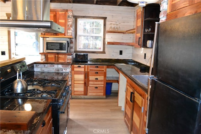 kitchen featuring island range hood, light hardwood / wood-style flooring, dark stone counters, black appliances, and wood walls