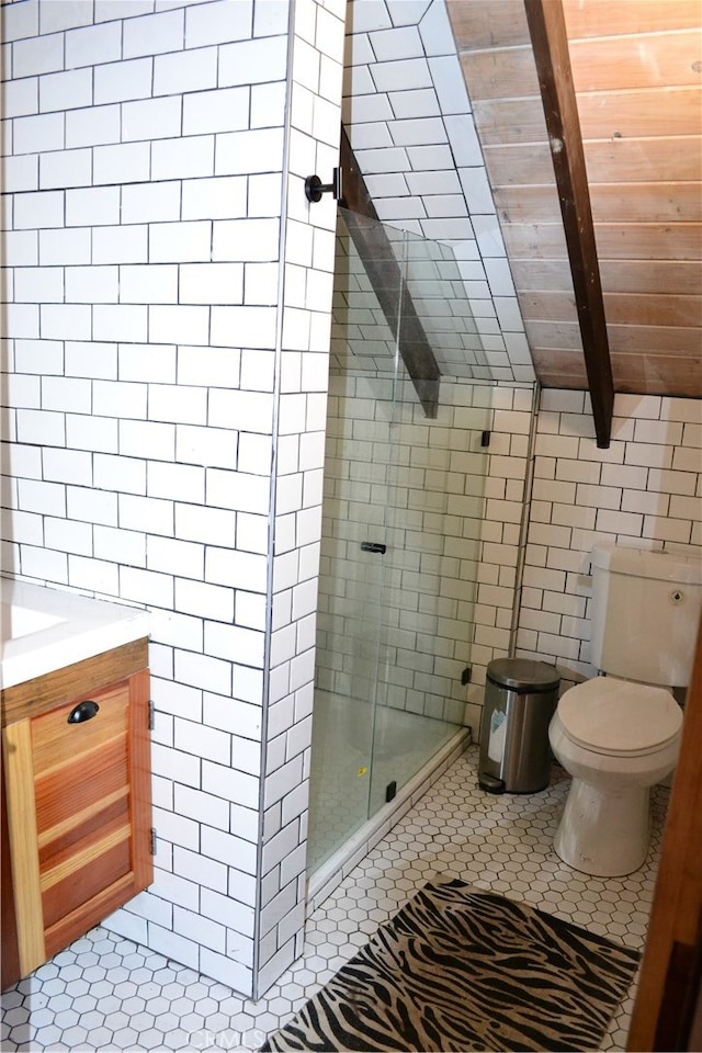 bathroom with tile patterned floors, toilet, a shower with shower door, vanity, and tile walls