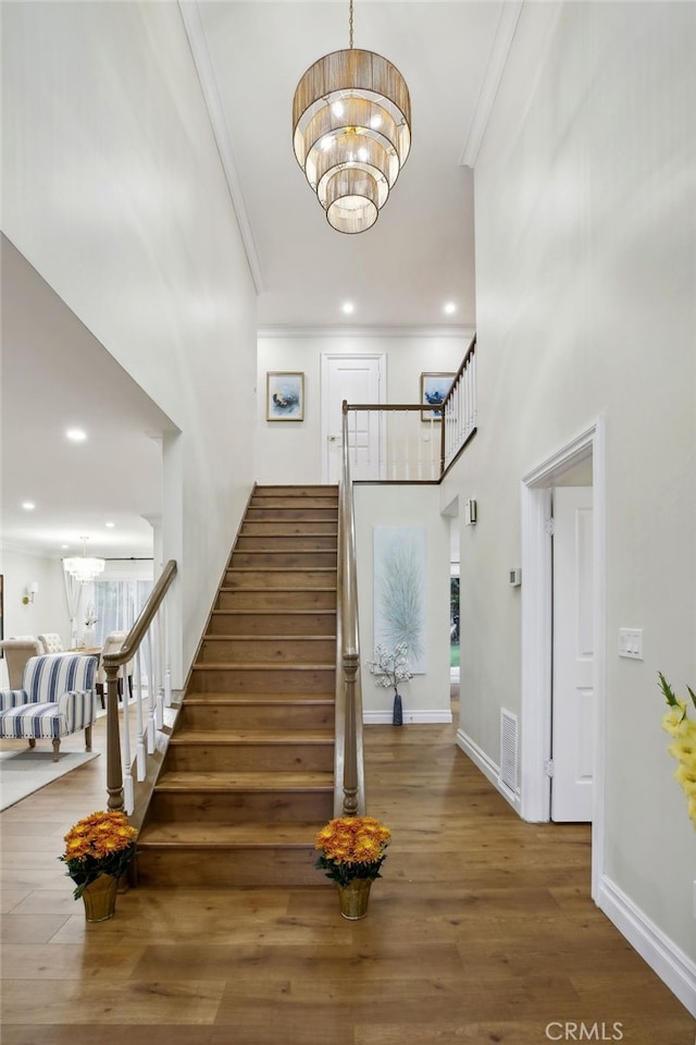 stairs featuring wood-type flooring, ornamental molding, and a notable chandelier