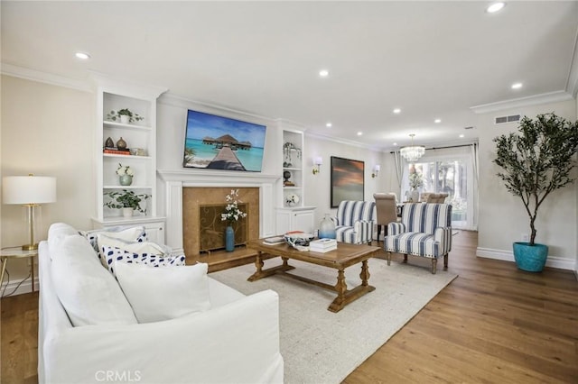 living room featuring crown molding, hardwood / wood-style floors, built in features, and a notable chandelier