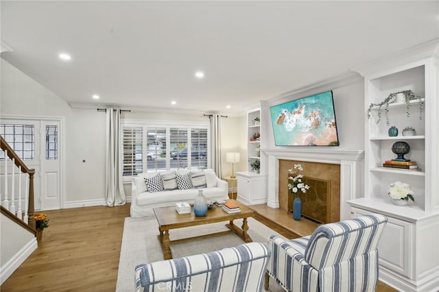 living room featuring built in shelves, light wood-type flooring, and crown molding