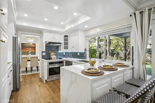 kitchen featuring appliances with stainless steel finishes, light wood-type flooring, tasteful backsplash, sink, and white cabinetry