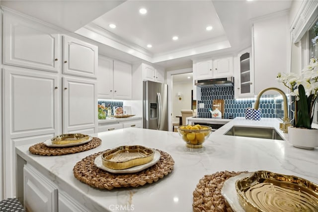 kitchen featuring light stone countertops, sink, stainless steel fridge with ice dispenser, a tray ceiling, and white cabinets