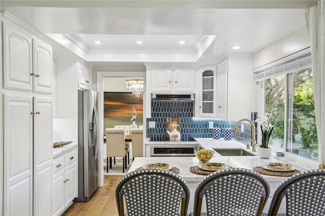 kitchen featuring stainless steel refrigerator with ice dispenser, light wood-type flooring, a tray ceiling, sink, and white cabinets