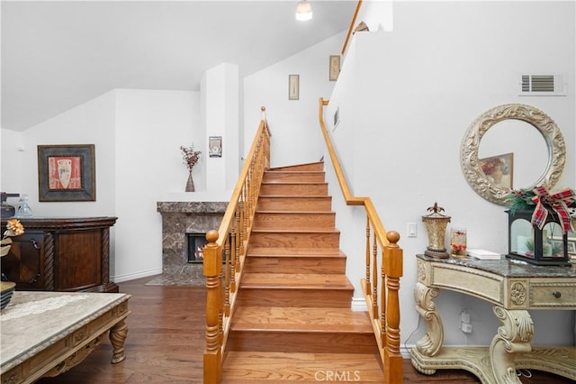 stairway with vaulted ceiling, a high end fireplace, and wood-type flooring