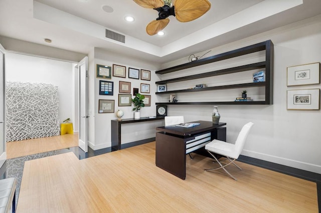 office space featuring ceiling fan, light hardwood / wood-style floors, and a tray ceiling