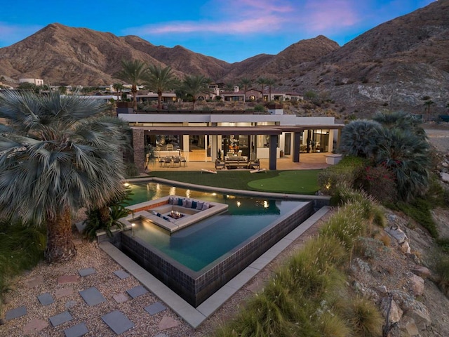 pool at dusk with an in ground hot tub, a mountain view, and a patio