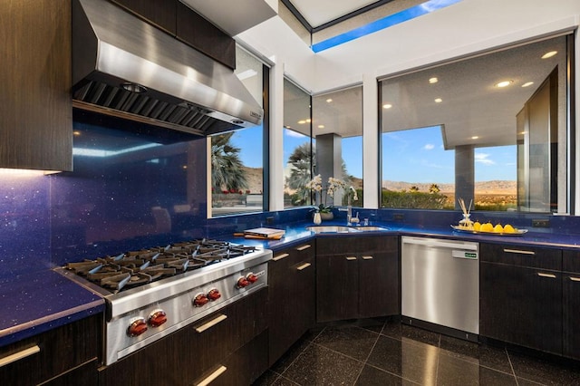 kitchen featuring decorative backsplash, appliances with stainless steel finishes, wall chimney exhaust hood, dark brown cabinetry, and sink