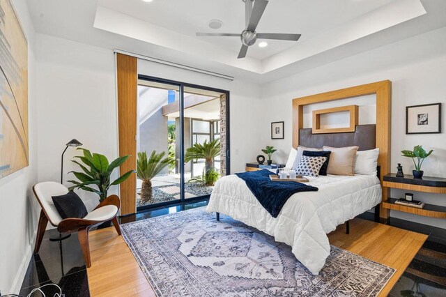 bedroom featuring access to outside, ceiling fan, hardwood / wood-style floors, and a tray ceiling