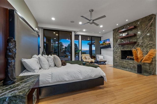 bedroom featuring access to exterior, ceiling fan, light hardwood / wood-style flooring, and a fireplace