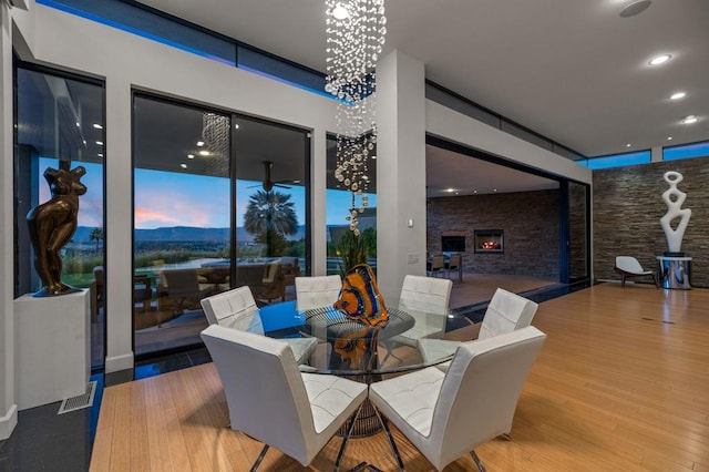 dining space with hardwood / wood-style flooring, a notable chandelier, and a stone fireplace