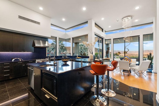 kitchen with dark wood-type flooring, an inviting chandelier, ventilation hood, an island with sink, and black microwave