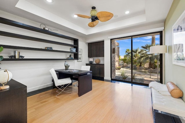 office space with a tray ceiling, light hardwood / wood-style flooring, and ceiling fan