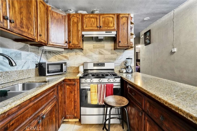 kitchen with tasteful backsplash, light stone counters, sink, and appliances with stainless steel finishes