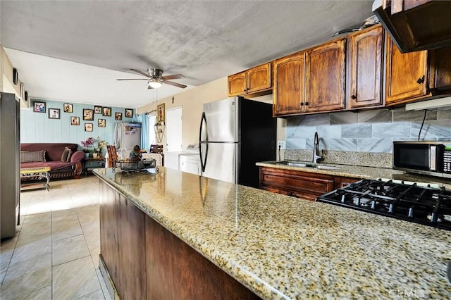 kitchen with light stone countertops, appliances with stainless steel finishes, ceiling fan, exhaust hood, and sink