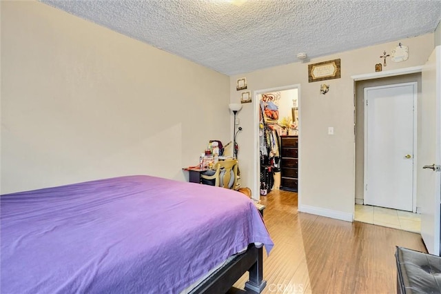 bedroom featuring a walk in closet, a closet, hardwood / wood-style floors, and a textured ceiling