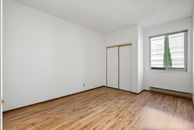 unfurnished bedroom with a textured ceiling, light wood-type flooring, a baseboard radiator, and a closet