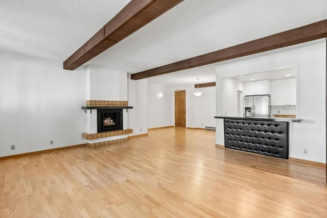 unfurnished living room with beamed ceiling, light wood-type flooring, a textured ceiling, and a baseboard radiator