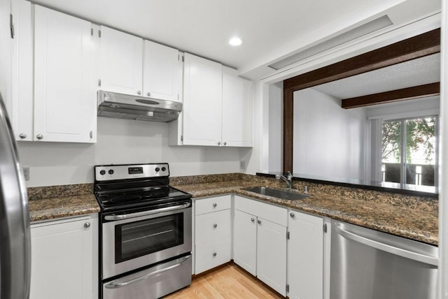 kitchen with stainless steel appliances, white cabinetry, dark stone counters, and sink