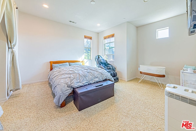 carpeted bedroom with heating unit and multiple windows