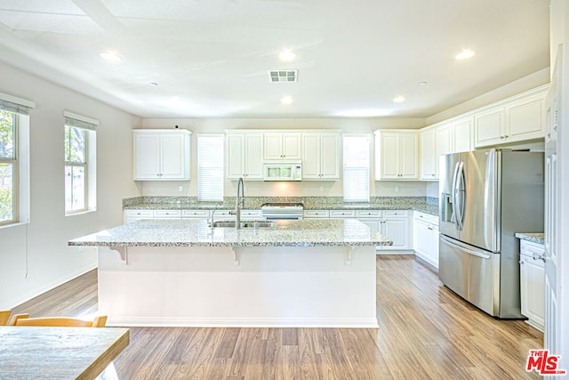 kitchen featuring a kitchen bar, a center island with sink, stainless steel fridge, white cabinets, and sink