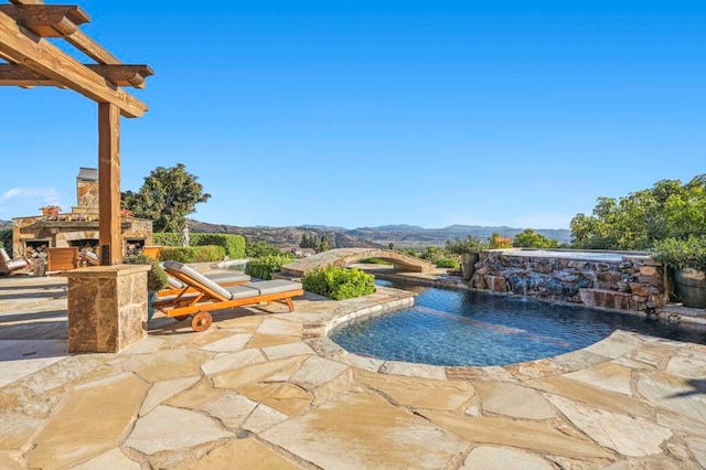 view of swimming pool featuring a patio area, a mountain view, pool water feature, and an outdoor stone fireplace