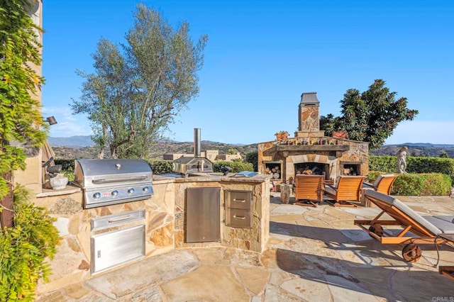 view of patio featuring a mountain view, an outdoor stone fireplace, area for grilling, and a grill